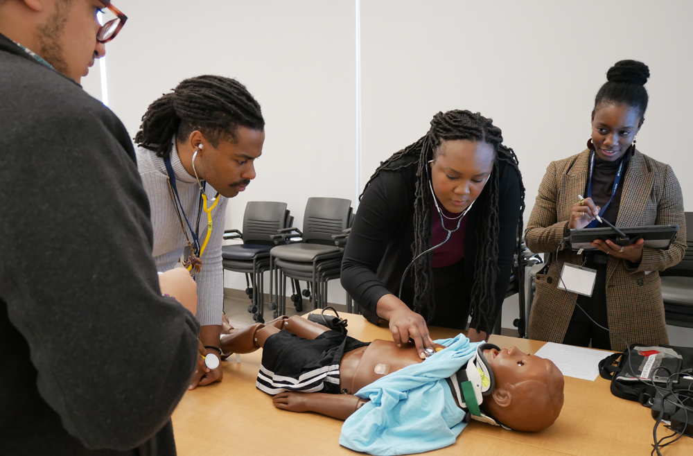 At Med Immersion Day, Claudia Gambrah-Lyles, MD (far right) facilitates medical simulations, assessing a student interpreting changes in vital signs on the mannequin of a 5-year-old trauma patient.
